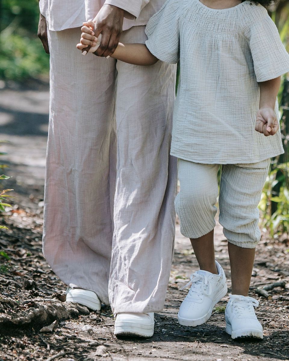 A parent and a young child walking hand in hand along a sunny garden path